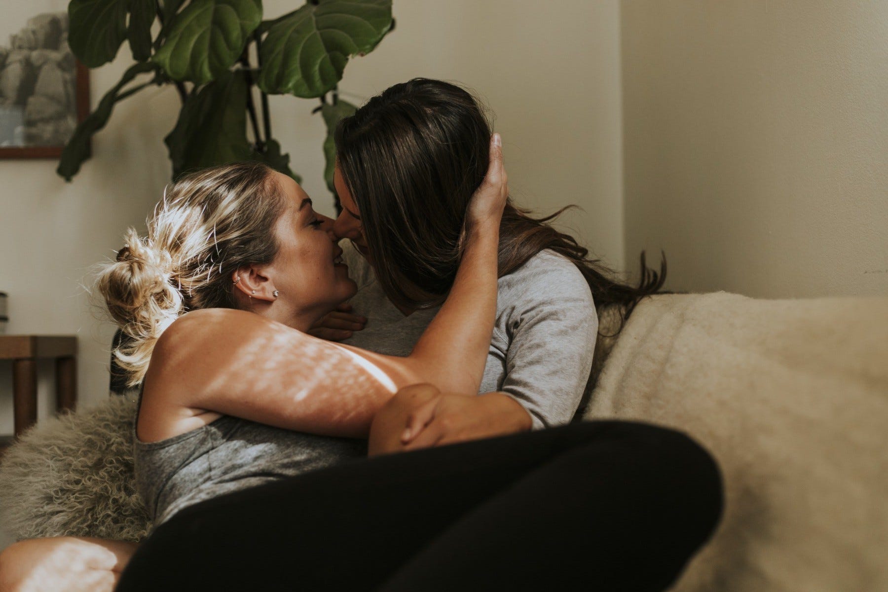 Girlfriends smiling and kissing on a couch