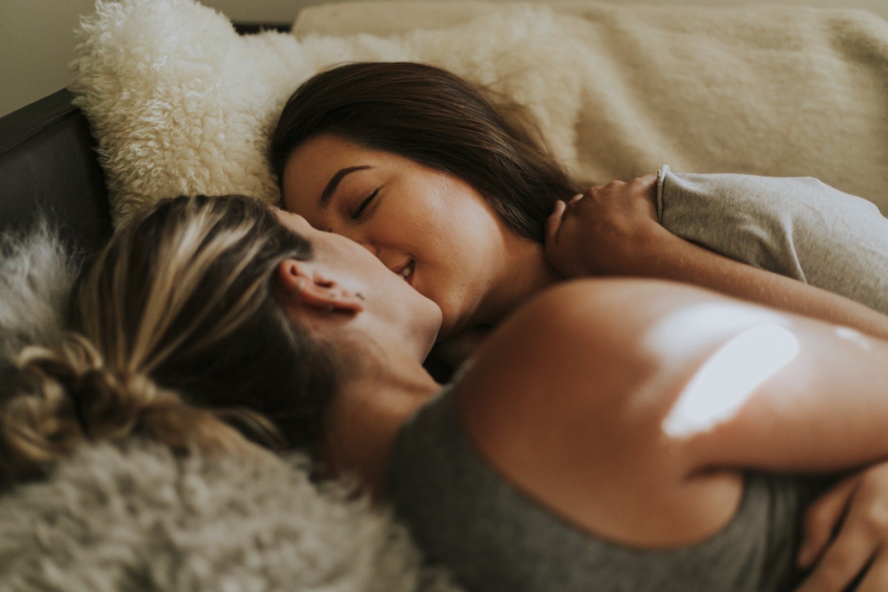 Two women kissing and smiling in bed